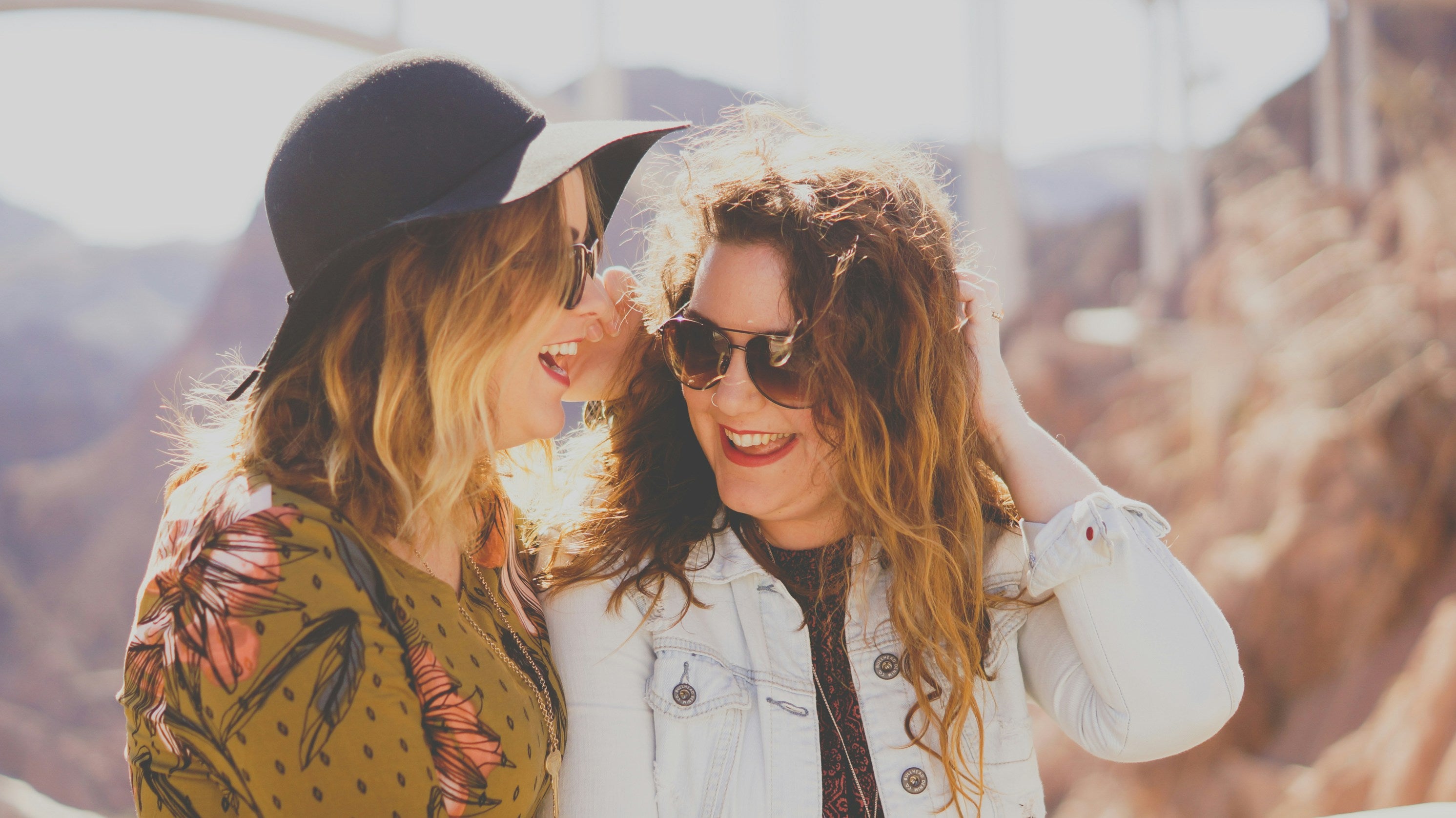 Two women standing close together outdoors with mountains in the background