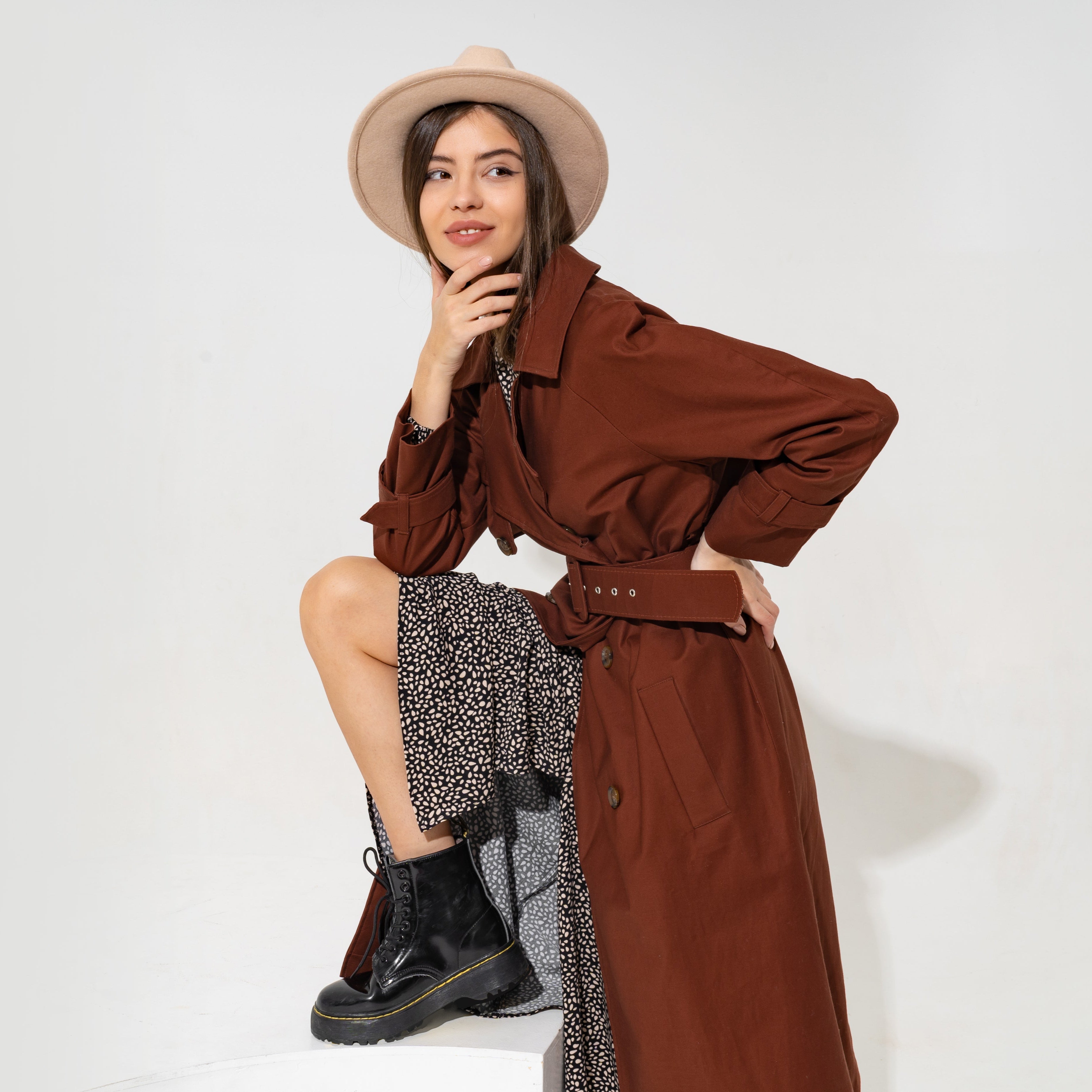 Woman wearing a brown trench coat and black boots on a white background