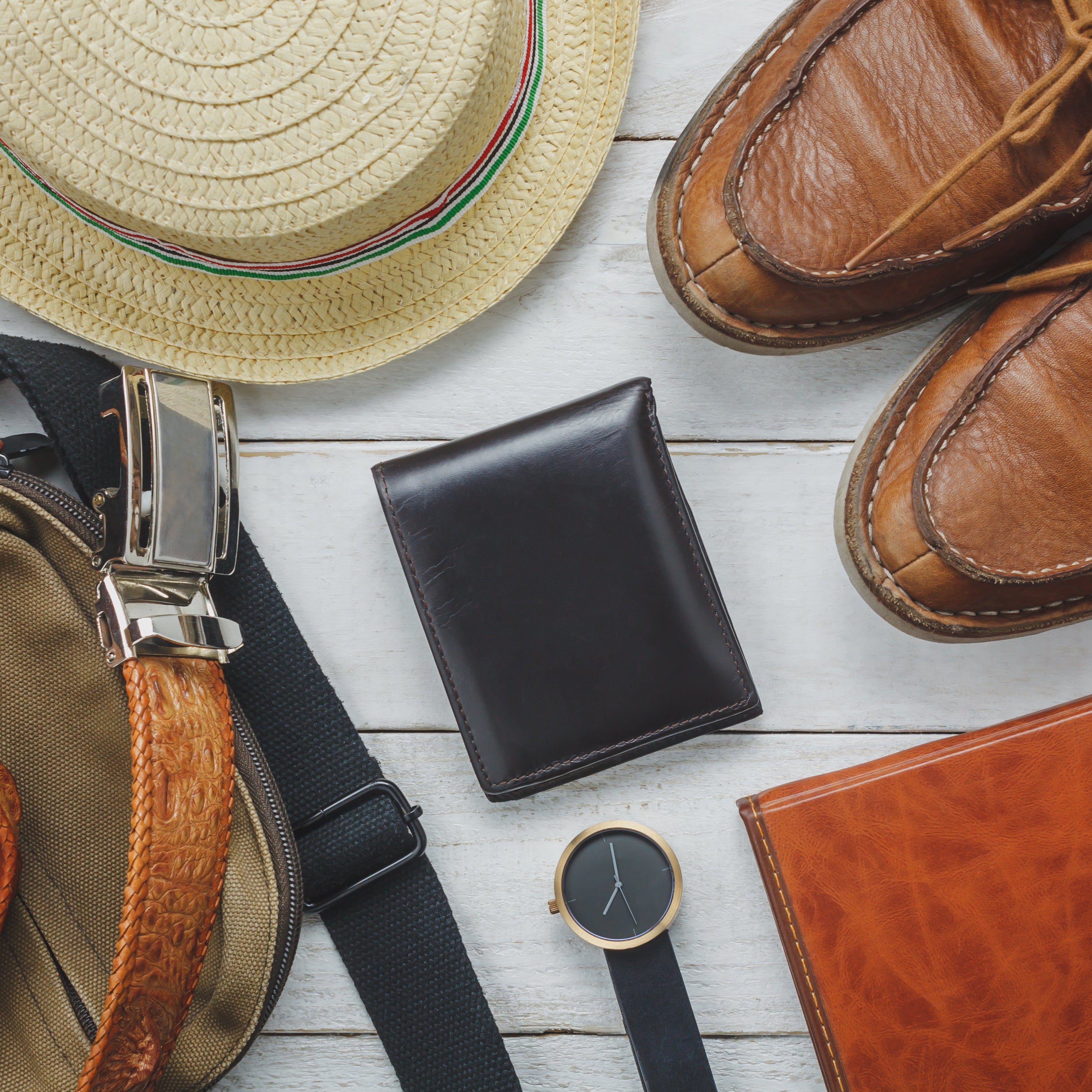 Collection of men's accessories including a hat, shoes, belt, wallet, and watch on a wooden surface.
