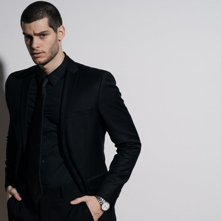 Man wearing a black suit against a plain background
