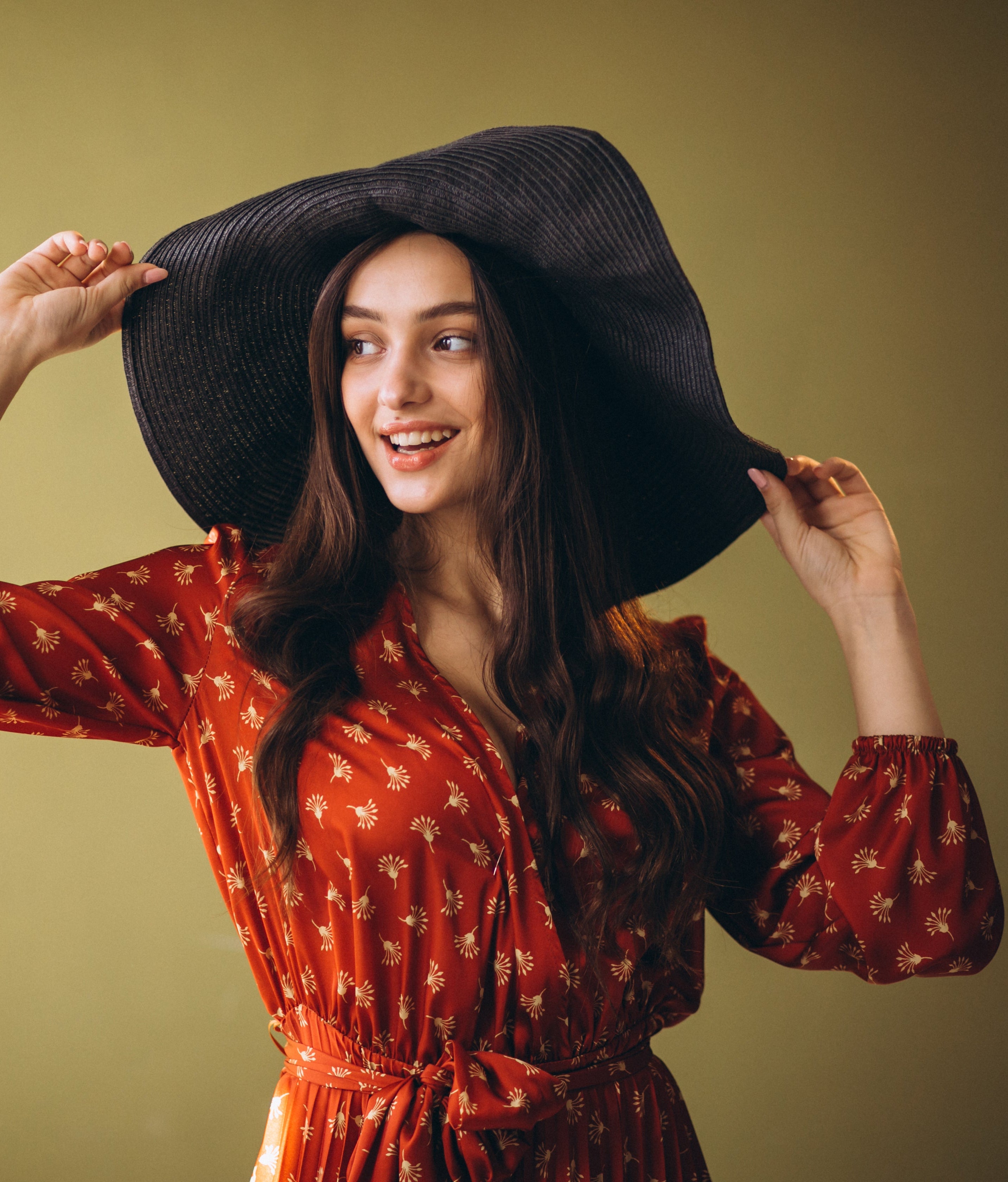 Woman wearing a red dress and black hat against a yellow wall